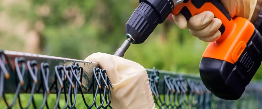 Man installing chain link fence with a screwdriver