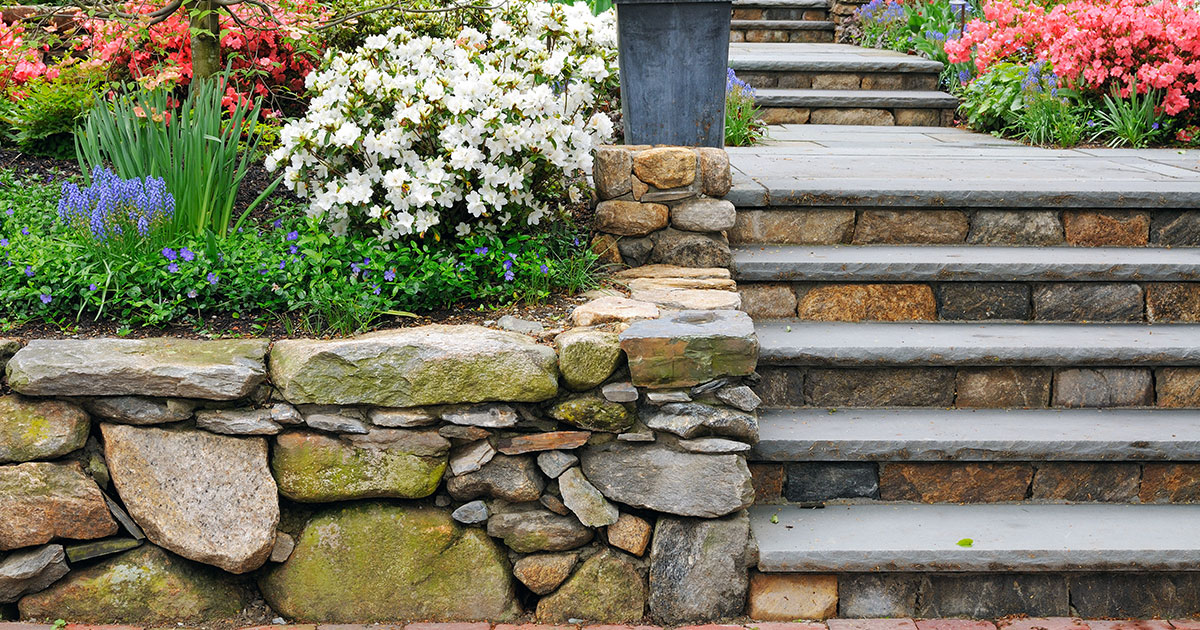 A small retaining wall made of stone with flowers and a few stairs