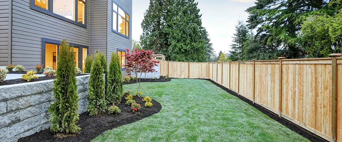 A wooden privacy fence with a patch of grass near a home