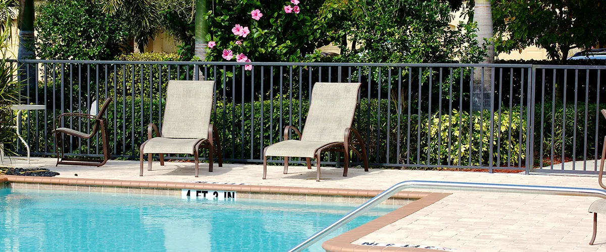 A black metal fence with two long chairs and a pool