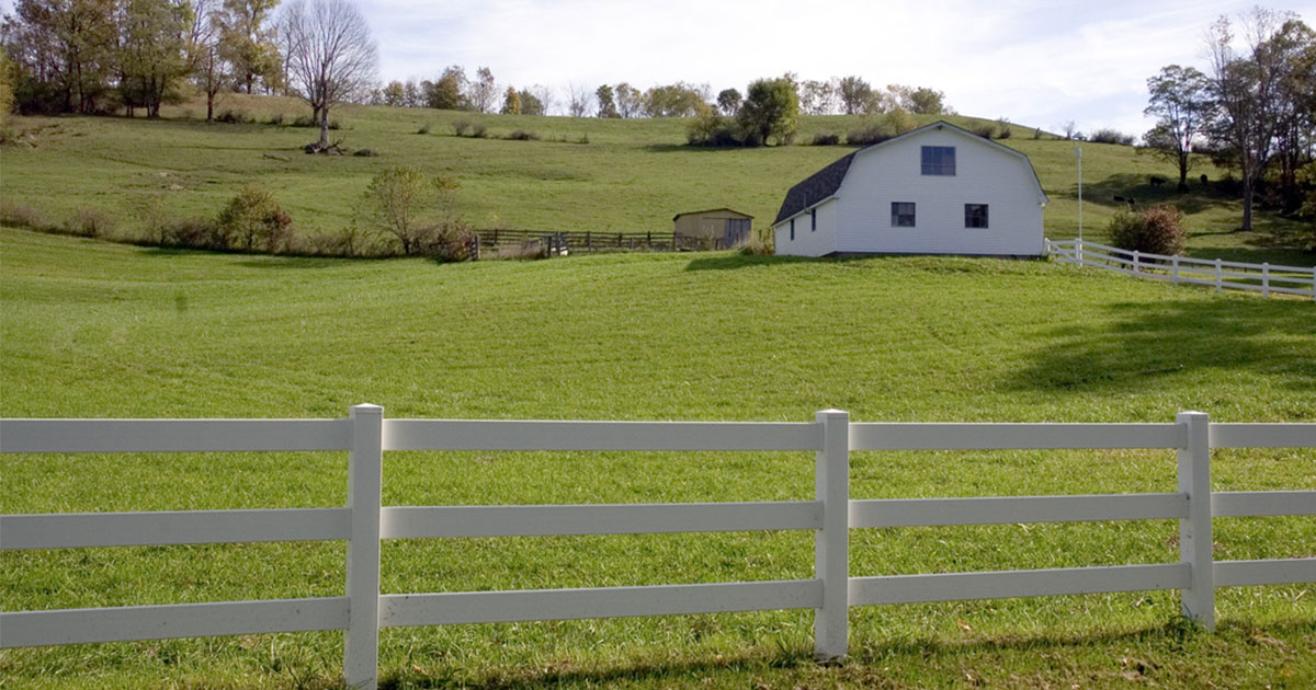 A green field with a white rail fence and a farm house