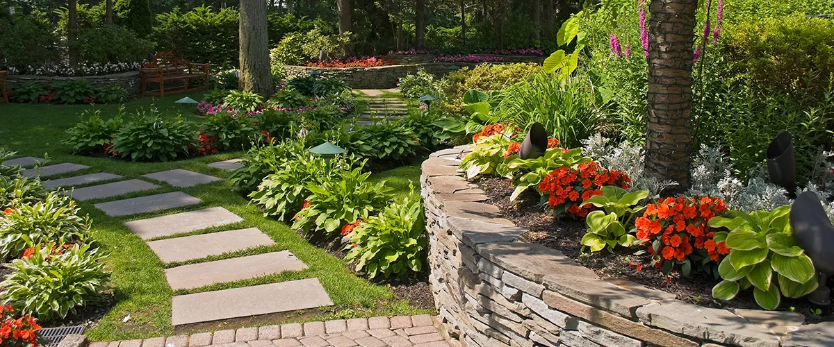 A garden with stone pavement and a retaining wall with red flowers