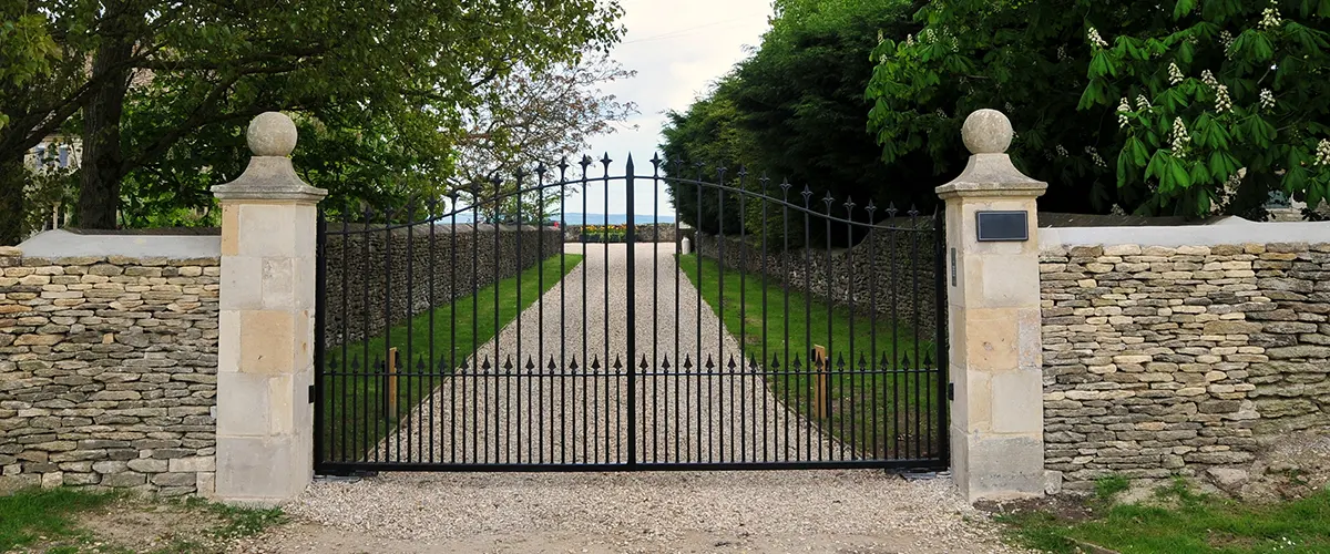 A metal gate with stone walls and a long driveway