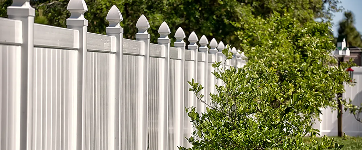 White panel of vinyl fencing and a small tree near it