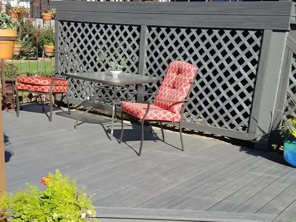 A dark composite decking with two red chairs and a glass table